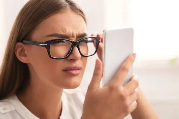Photo of Girl Looking At Cellphone Through Eyeglasses Having Vision Problem Indoor
