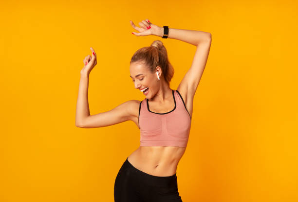 donna in auricolari wireless che balla ascoltando musica, sfondo giallo - fitness apparel foto e immagini stock