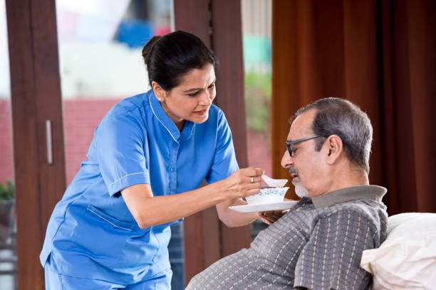 Nurse feeding food to old man on bed Female nurse feeding food to senior patient on bed india hospital stock pictures, royalty-free photos & images