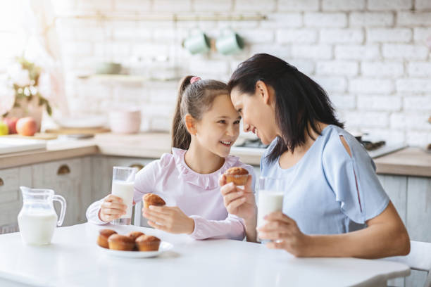 istock Mother and daughter eating cupcakes and drinking milk in kitchen. 1178537506