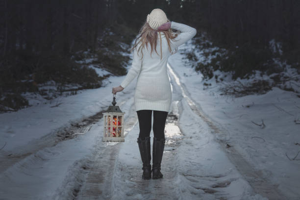Woman walking along an icy road through forest in winter and holding a lantern