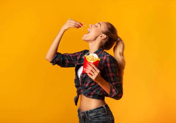 Young Woman Eating French-Fries On Yellow Background Hungry Young Woman Eating French-Fries On Yellow Studio Background. Cheat Meal Concept potato chip photos stock pictures, royalty-free photos & images