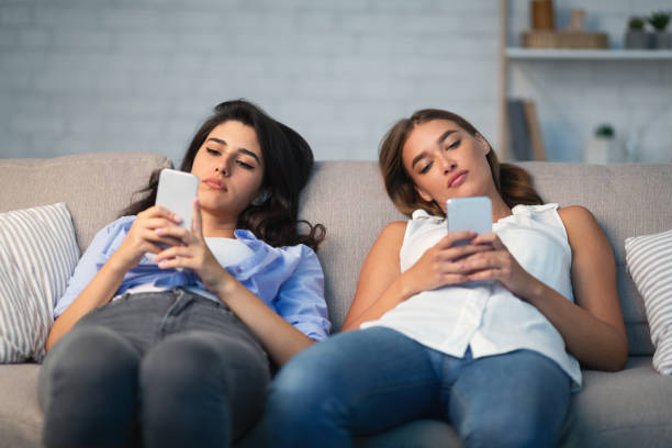 istock Two Girls Using Smartphones Sitting On Couch Indoor 1178543850