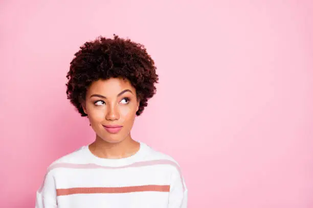 Photo of curious sly black skinned girl glancing at empty space wearing striped white, sweater planning her life isolated over pink pastel color background