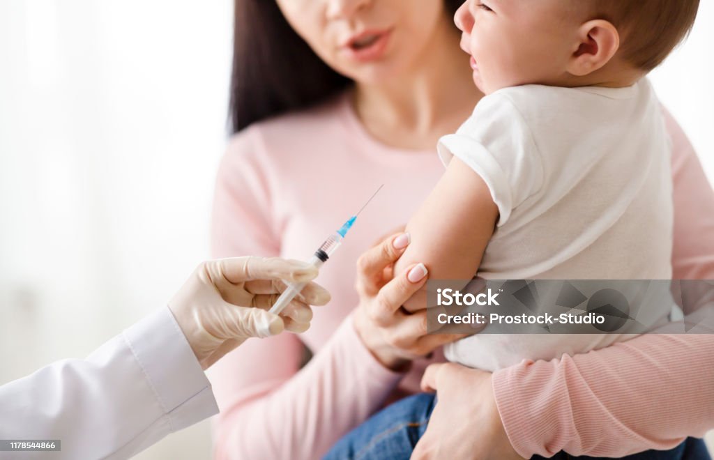 Doctor giving intramuscular injection to little baby Vaccination and immunity strengthening. Doctor giving intramuscular injection to little baby in arm Vaccination Stock Photo