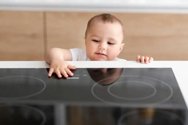 Hazard at kitchen. Curious toddler reaching hand to hot electric cooktop, free space