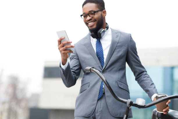 istock Happy afro entrepreneur using phone, standing with bicycle outdoors 1178546763
