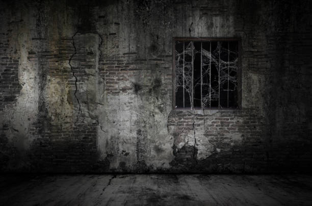 刑務所の古いレンガの壁とほこりっぽい床にコブウェブやクモの巣で覆われた窓と錆びたバー ストックフォト