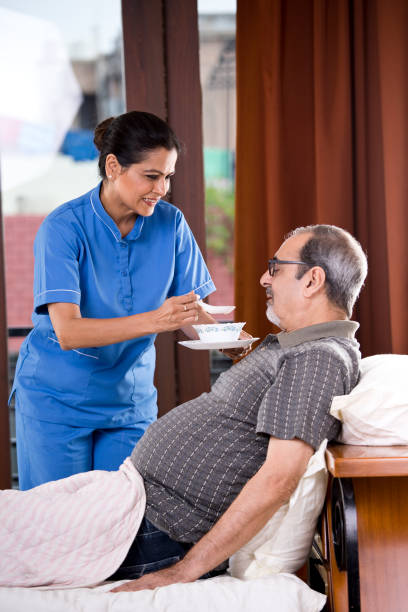 nurse feeding food to old man on bed - senior adult nursing home eating home interior imagens e fotografias de stock