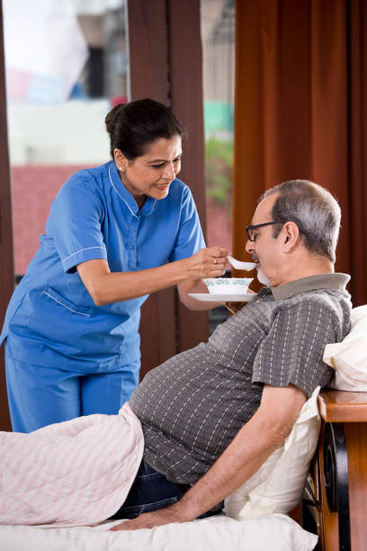 nurse feeding food to old man on bed - senior adult nursing home eating home interior imagens e fotografias de stock