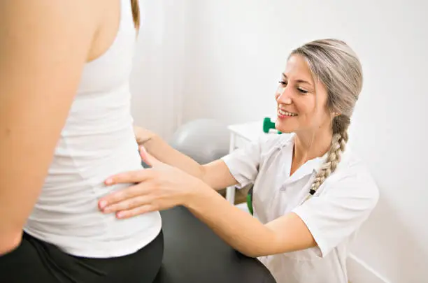 Photo of A Modern rehabilitation physiotherapist at work with client. working on lower back.