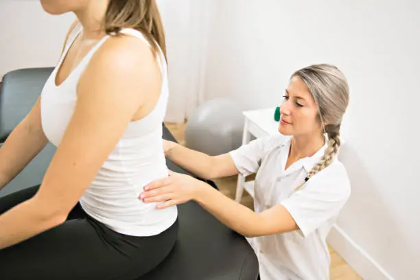 Photo of A Modern rehabilitation physiotherapist at work with client. working on lower back.