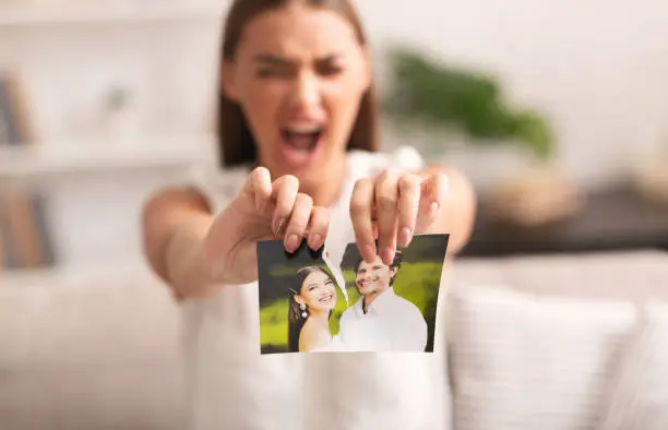 Divorce. Angry Woman Ripping Wedding Photo With Ex-Husband After Breakup Indoor. Selective Focus