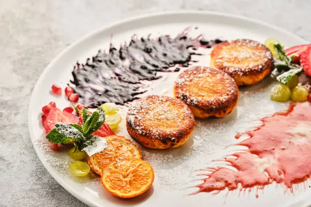 Photo of Cottage cheese pancakes, syrniki, curd fritters with fresh berries, grapes and orange.
