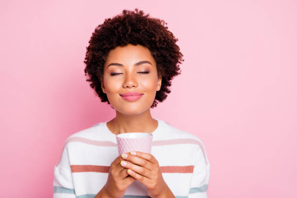 Photo of pretty dark skin lady holding in hands hot beverage cup dreamy closing eyes enjoy good smell wear striped pullover isolated pastel pink color background Photo of pretty dark skin lady holding in hands hot beverage cup dreamy, closing eyes enjoy good smell wear striped pullover isolated pastel pink color background pink tea stock pictures, royalty-free photos & images