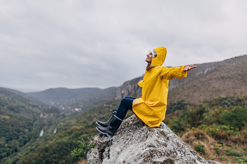 One woman, sitting on mountain on a rainy day in yellow raincoat.