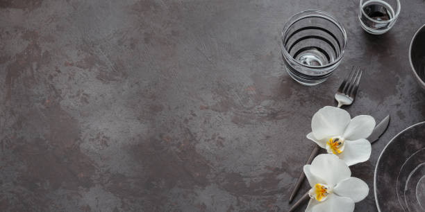 istock Elegance table setting with knitted grey napkin, cutlery, ceramic plates, glasses and white orchid flowers 1178568581