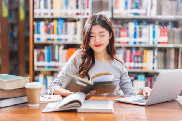 istock Asian young Student in casual suit doing homework and using technology laptop in library of university or colleage with various book and stationary over the book shelf background, Back to school 1178568713