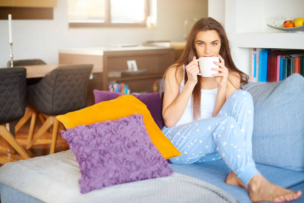 istock Beautiful young woman drinking morning tea while sitting on couch at home 1178568916