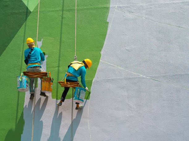 Painters painting exterior of building Chiang Rai, Thailand: September 18, 2019 - Two painters are painting the exterior of the building on a dangerous looking scaffolding hanging from a tall building. outdoor elevator stock pictures, royalty-free photos & images