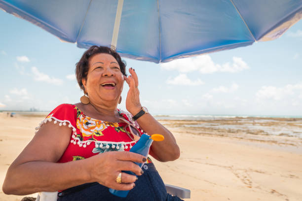 mujer mayor usando una loción bronceadora en la playa - crema de sol fotografías e imágenes de stock