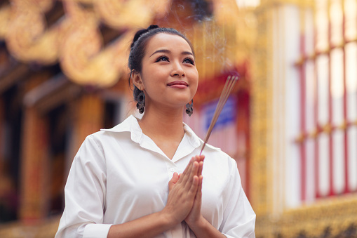 A woman visits a buddhist temple in Chiang Mai, Thailand, holding incense sticks.