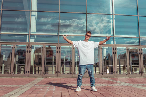 Man athlete, guy dancer in summer city. Glasses on background of glass windows. Fashionable modern break dance style, fitness sport hip hop. Urban culture, street dance. In t-shirt jeans sneakers. stock photo