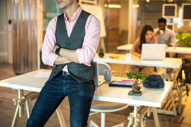 Unrecognizable businessman sitting on desk at work with crossed arms
