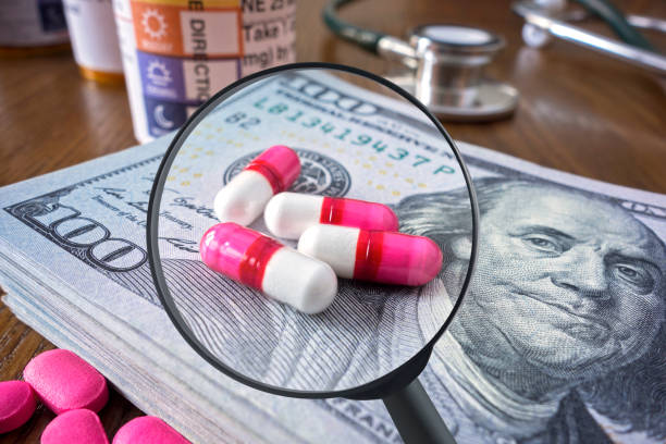 The search for right medication Looking at medicine pills on a pile of 100 dollar bills with a magnifying glass big pharma stock pictures, royalty-free photos & images