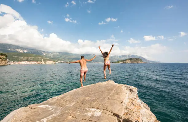 Photo of Young adventurous couple cliff jumping into beautiful sea.