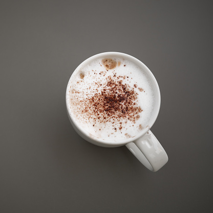 Cappuccino. Cup of coffee with milk foam and cinnamon stands on a gray table, top view. Close-up square photo
