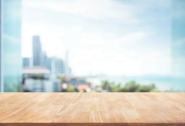 Wood table top on blur window glass,wall background with city view.For montage product display or design key visual layout