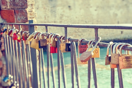 Horizontal photo of many color metal locks placed on the old fence. The locks have signatures and messages from lovers in the ancient town Sirmione in Italy next to castle.