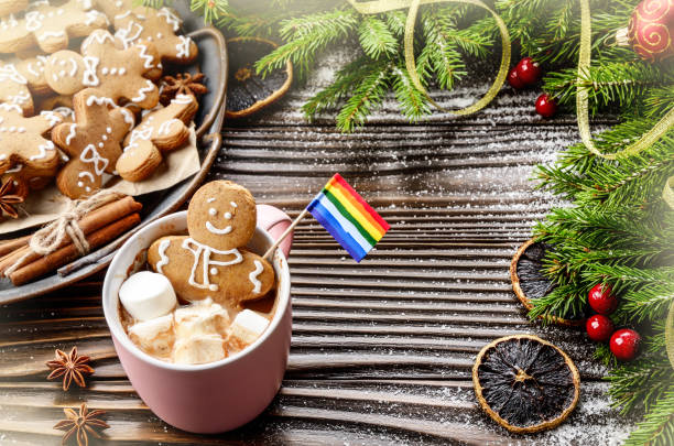 istock Pink mug with hot chocolate marshmallows and gingerbread man with rainbow flag on background of spruce branch and tray with cookies 1178585771