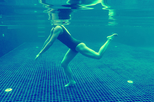 Woman in black swimsuit dancing posing swimming underwater on blue tiles background.