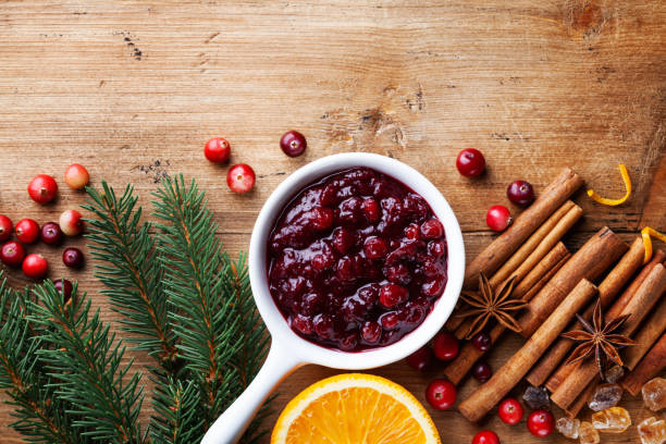 Cranberry sauce in ceramic saucepan with ingredients for cooking decorated with fir tree for Christmas or Thanksgiving day on wooden kitchen table. Top view. Cranberry sauce in ceramic saucepan with ingredients for cooking decorated with fir tree for Christmas or Thanksgiving day on wooden kitchen table. Top view with copy space. sauces table turkey christmas stock pictures, royalty-free photos & images