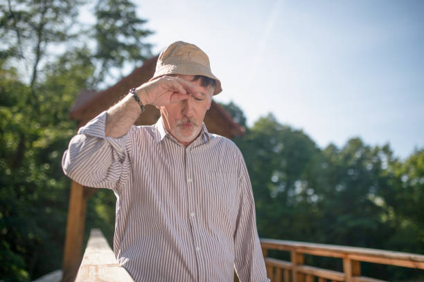 Bearded mature man wearing summer hat having headache