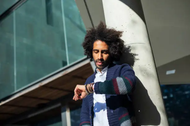 Young handsome man with afro hair Checking the time on wrist watch, relaxed and confident