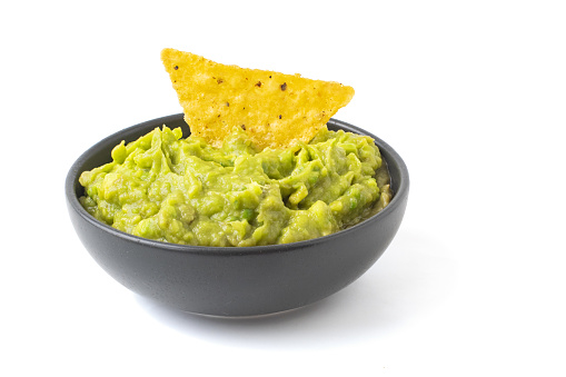 Green Guacamole with nachos in dark bowl isolated on white background.