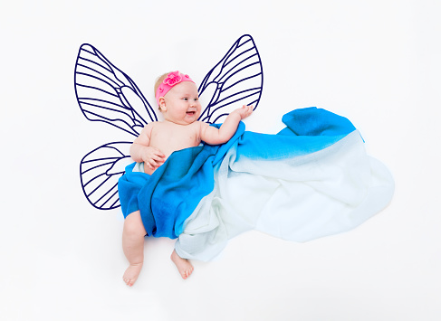 Laughing baby girl wrapped in fabric on a cloud with painted butterfly wings