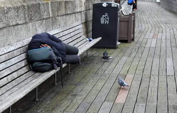 Anonymous person sleeping on River Liffey boardwalk bench, in Dublin city centre, Ireland.