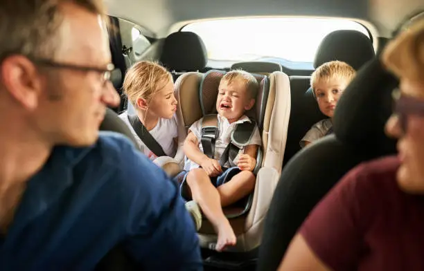 Shot of a little boy crying in backseat of a car with his sister and parents looking at him and trying to comfort him