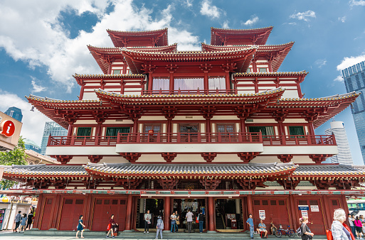 Singapore - March 22, 2019: Chinatown. Main entrance maroon-red facade of Buddha Tooth Relic Temple and Museum under blue sky with white clouds. People in front.
