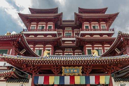 Singapore - March 22, 2019: Chinatown. Fish eye view on pagoda-like structure of main entrance maroon-red facade of Buddha Tooth Relic Temple under gray cloudscape.