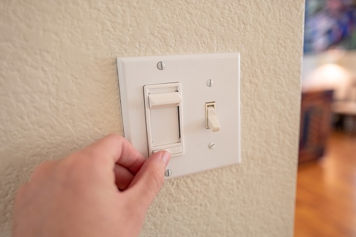 Close-up, personal perspective or point of view of human hand of a man adjusting dimmer switch on wall light switch, September 24, 2019