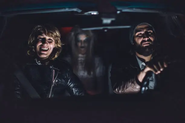 Young couple sitting in car with a scary witch/ghost/demon/monster/zombie behind them
