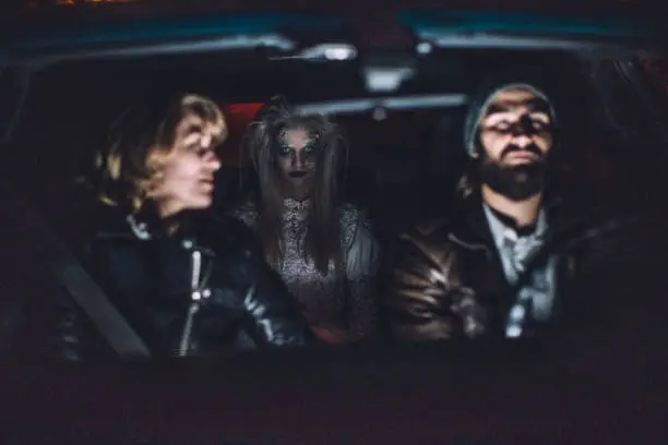 Young couple sitting in car with a scary witch/ghost/demon/monster/zombie behind them