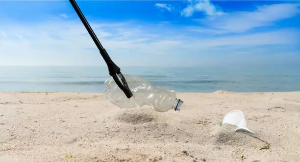 concept about pollution collecting plastic garbage with tongs on a beach