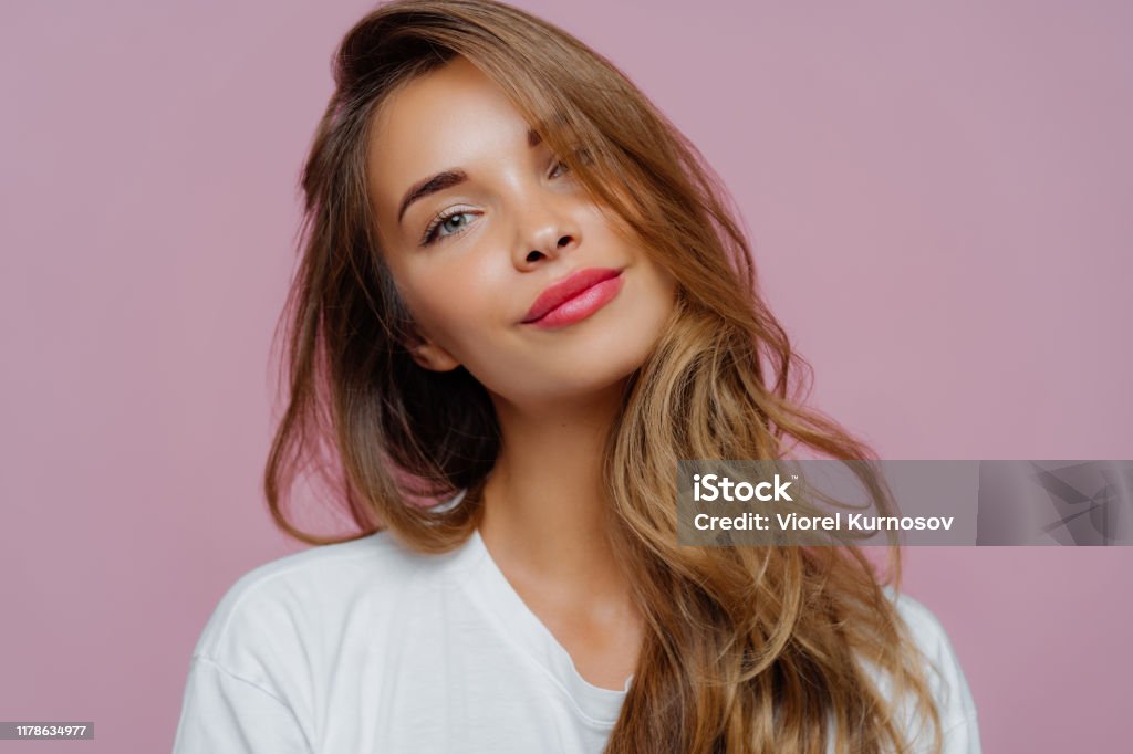 Portrait Of Satisfied Relaxed Young Female Model Tilts Head Has Makeup Fair  Hair Dressed In White Clothes Poses Against Purple Background Has Well  Cared Complexion People Beauty Face Care Stock Photo -