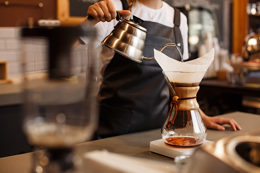 Professional barista preparing coffee using glass coffeemaker pour over coffee maker and drip kettle.